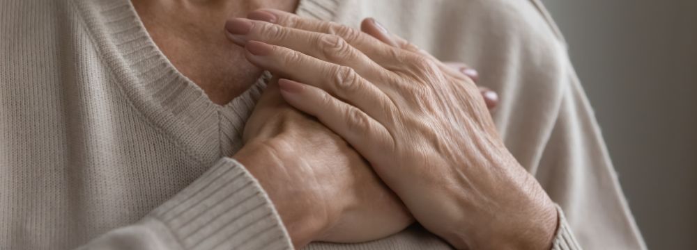 Widowed woman clutches her chest as she grieves and suffers from broken heart syndrome