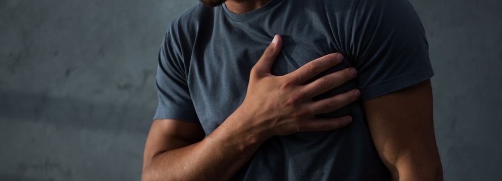 A man holds his chest wondering if the chest pain he is experiencing is serious and needs medical attention