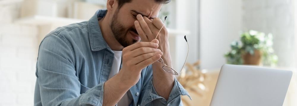 man rubbing his eyes showing signs of fatigue in front of his laptop