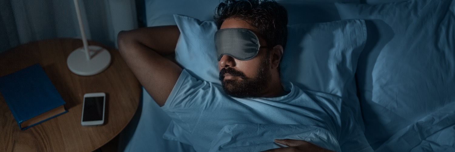 Man lying in bed sleeping with eye mask on face 